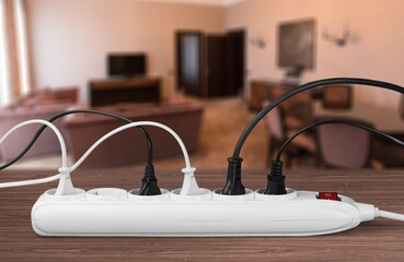Unplugged electric appliance plug over switched off white power strip on the floor. Increasing the...
