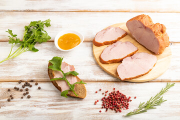 Smoked pork ham on cutting board on white wooden background. Side view, close up.