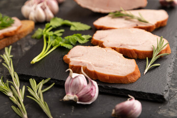 Smoked pork ham on cutting slate board on black concrete background. Side view, close up, selective focus.