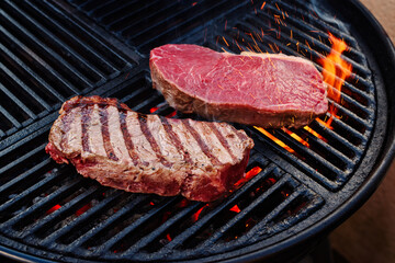 Raw dry aged wagyu roast beef steak grilled as close-up on a charcoal grill with fire and smoke