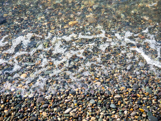 Wave on a pebbly shore. Surf. Bathing place. Nature of the south. Close-up of the coastline