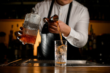 process of preparing cocktail at bar. Bartender pours a drink into a glass