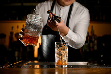 Close-up view on process of preparing cocktail at bar. Bartender pours a drink into a glass