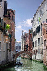 Romantic view on narrow street of Venice with old buildings and bridge above a canal. Boat float on the water, sunny day blue sky. Italian holidays.