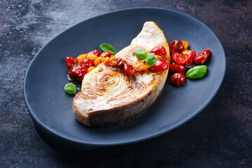 Fried swordfish steak with tomatoes and paprika served as close-up on a design plate - obrazy, fototapety, plakaty
