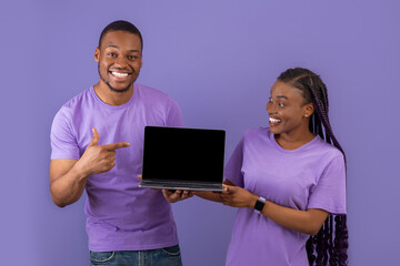 Excited black couple showing black blank laptop screen