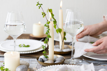 Rustic zero waste wedding decor with natural elements. Wooden table, candles, linen napkins, branches with green leaves. Eco-friendly decoration for the special dinner. Romantic and cozy place