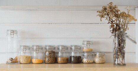 A row of glass jars of groceries and a bouquet of dried flowers are on the table. Scandinavian design idea, food storage, zero waste