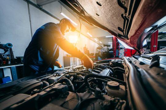 Young Mechanic Checking Engine Oil Level In Modern Car. Auto Car Repair Service Center. 