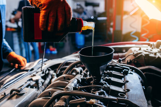 Close up hand of auto mechanic technician replacing and pouring motor oil in modern automobile engine at auto repair service station.