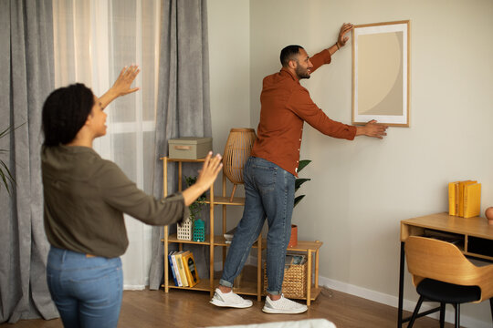 Black Couple Hanging Poster In Frame On Wall At Home