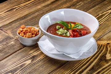 Raw tomato soup, typical food of Spain, served in white bowls with pieces of tomato, cucumber and paprika. Wooden background