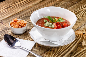 Raw tomato soup, typical food of Spain, served in white bowls with pieces of tomato, cucumber and paprika. Wooden background
