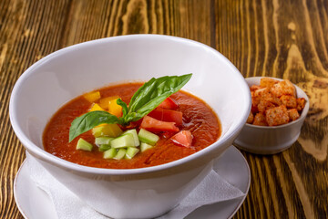 Raw tomato soup, typical food of Spain, served in white bowls with pieces of tomato, cucumber and paprika. Wooden background