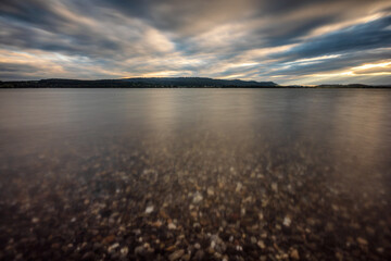Steine im Sonnenuntergang am Bodensee mit kraftvollen Wolken im Hintergrund am Himmel