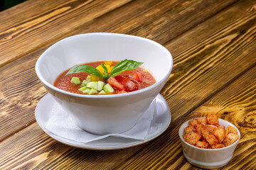 Raw tomato soup, typical food of Spain, served in white bowls with pieces of tomato, cucumber and paprika. Wooden background