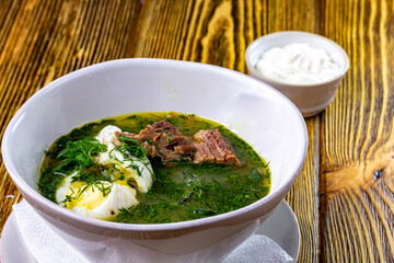 Green Sorrel soup with with boiled eggs wedges in white bowl. Selective focus, bunch of fresh sorrel on background