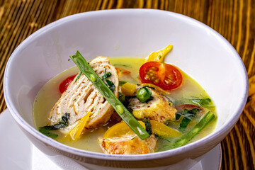 Vegetable soup with chicken rolls is a soup with the main ingredients of carrots, broccoli, celery and green onions, and sliced chicken rolls. Served in a black bowl on the table. Selective focus