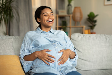 Joyful Pregnant Black Lady Touching Belly Sitting On Sofa Indoors