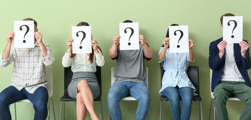 Young people holding paper sheets with question marks while sitting on chairs. Job interview concept