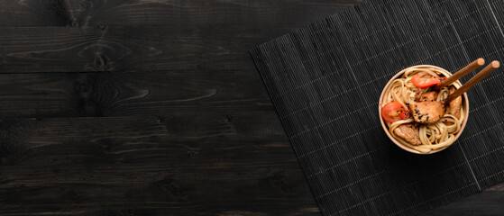 Paper bowl with tasty Chinese noodles and meat on dark wooden background with space for text