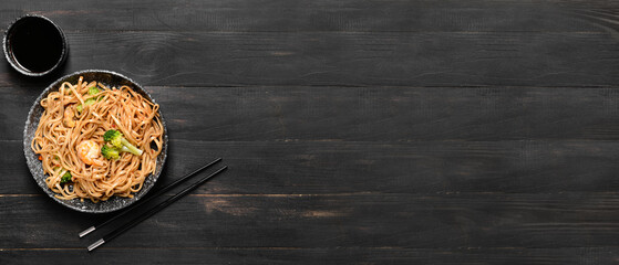 Plate with tasty Chinese noodles and seafood on dark wooden background with space for text
