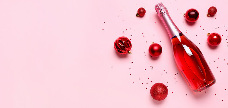 Bottle of champagne and Christmas balls on pink background with space for text