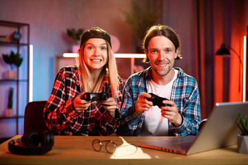Joyful young man and woman feeling happiness while winning in video games on laptop. Attractive happy couple enjoying entertainment at home during evening time.