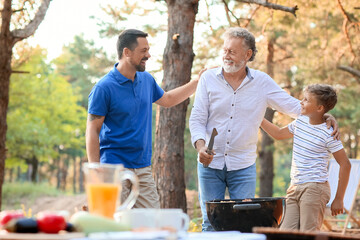 Senior man with his little grandson and son cooking food on grill at barbecue party