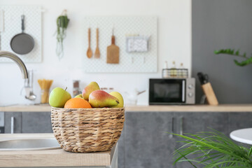 Wicker basket with fresh fruits on wooden counter in modern kitchen