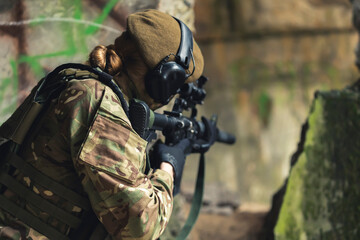 Fototapeta premium One single servicewoman aiming at target with firearm while wearing camouflage. Outdoor shot from the back. High quality photo