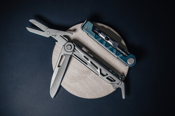 Detail product photo of a technical multitool with pliers, knife and other tools. Stainless multitool on black metal and wooden background.