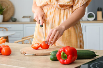 Pretty young woman cutting fresh tomato in kitchen, closeup