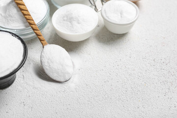 Bowls and spoon with baking soda on light background