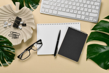 Modern keyboard, notebooks, eyeglasses and tropical leaves on yellow background