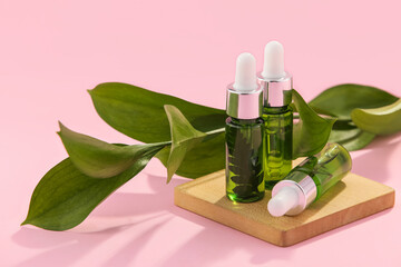 Bottles of natural serum and plant leaves on pink background