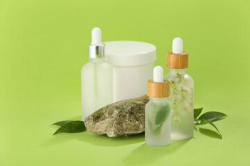 Fototapeta na wymiar Bottles of natural serum, stone and plant leaves on green background
