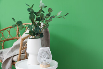 Vase with eucalyptus branches and lamp on table near green wall