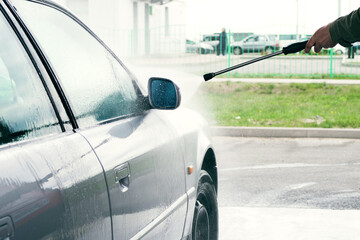 Self-service manual car wash. Driver washing a gray car with pressurized water at a car wash