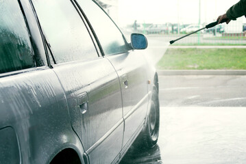 Self-service manual car wash. Driver washing a gray car with pressurized water at a car wash