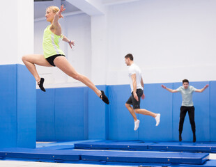 Focused female gymnast jumping on professional trampoline, practicing movements in jump during training..