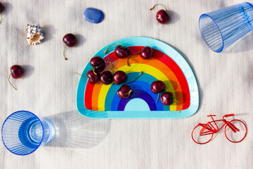 LGBTQ picnic in nature summer park. White plaid with dish in LGBT colors full of red cherries, blue...