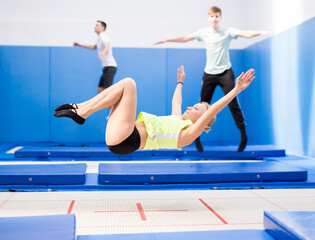 Smiling female gymnast jumping and bouncing on trampoline during workout in modern fitness center