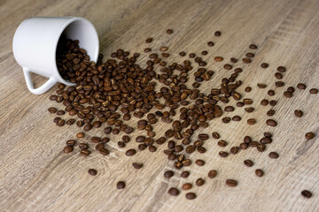 A cup filled with roasted coffee beans, which fell on the wooden table, scattered the coffee beans on the table.