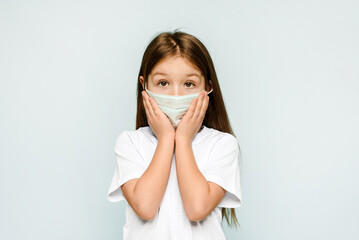 Frightened caucasian little girl is feeling surprised in a medical mask on a blue background. Copy space. Protection against viruses, coronavirus and pandemic.
