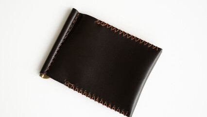 Empty brown men's money clip handmade leather wallet with a two pockets for cards lies on a white table. Selective focus, copy space, close up.