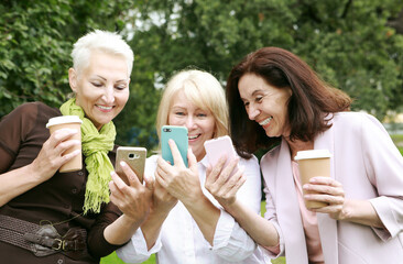 Fototapeta premium Charming old women laugh merrily and look at the screens of their smartphones.