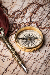 Old feather pen and golden compass on the antique mundi map.