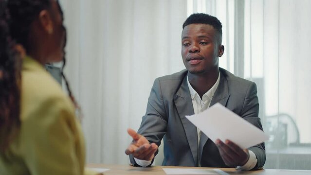 Making a first impression. Young black man meets potential employer in office for interview. Welcome to the company. Smiling black woman sitting at office desk and talking to during job interview