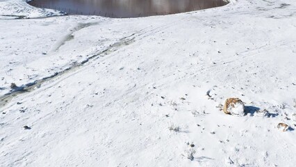 Mt Hermon, Israel. Fly in drone shot over a snowy valley to a crater lake, Birkat Ram. Hikers can be seen around the lake. Background is snow covered mountains and blue sky.